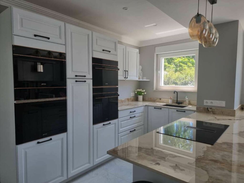 Cuisine sur mesure de style classique avec façades blanches moulurées en bois massif, îlot central et plan de travail en céramique, réalisée par Vibra Home Concept.